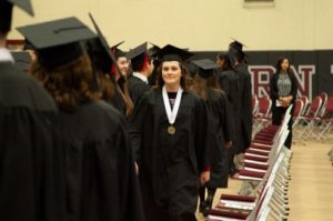 In a line of graduates, one woman smiles and faces the camera