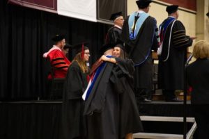 coming off of the stage, a woman is congratulated with a hug with a professor