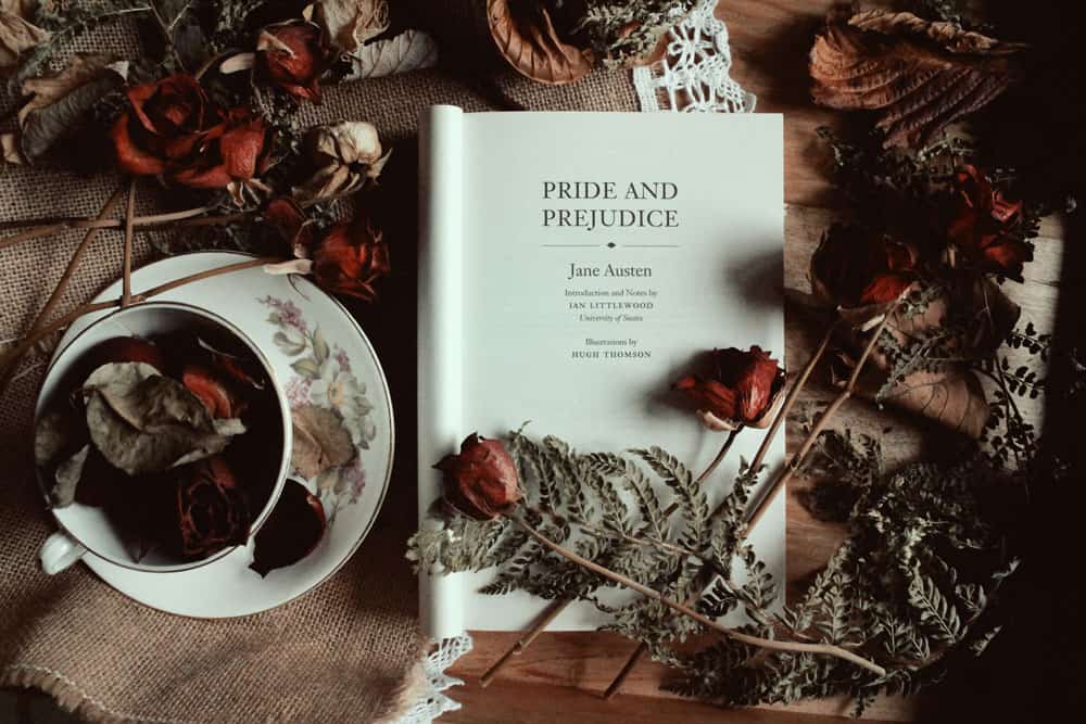 Book open to cover page of "Pride and Prejudice" book surrounded by roses and a cup of tea on a table