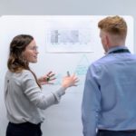 two people in front of white board
