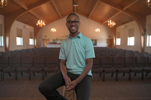 Jason Crocker sitting on a stool, smiling at camera with an empty church auditorium behind him