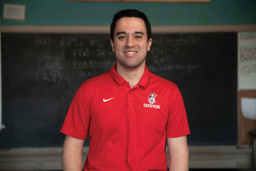 Matthew Valverde wearing a red polo standing in front of a schoolroom chalkboard