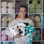 photo of Sabrina holding three stuffies standing in front of a wall of yarn