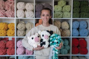 photo of Sabrina holding three stuffies standing in front of a wall of yarn