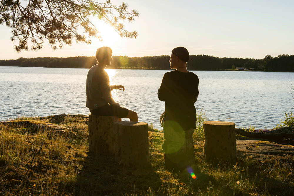two people sitting next to a lake at sunset and talking