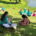 teen student sharing the gospel with a child on a grassy hill w